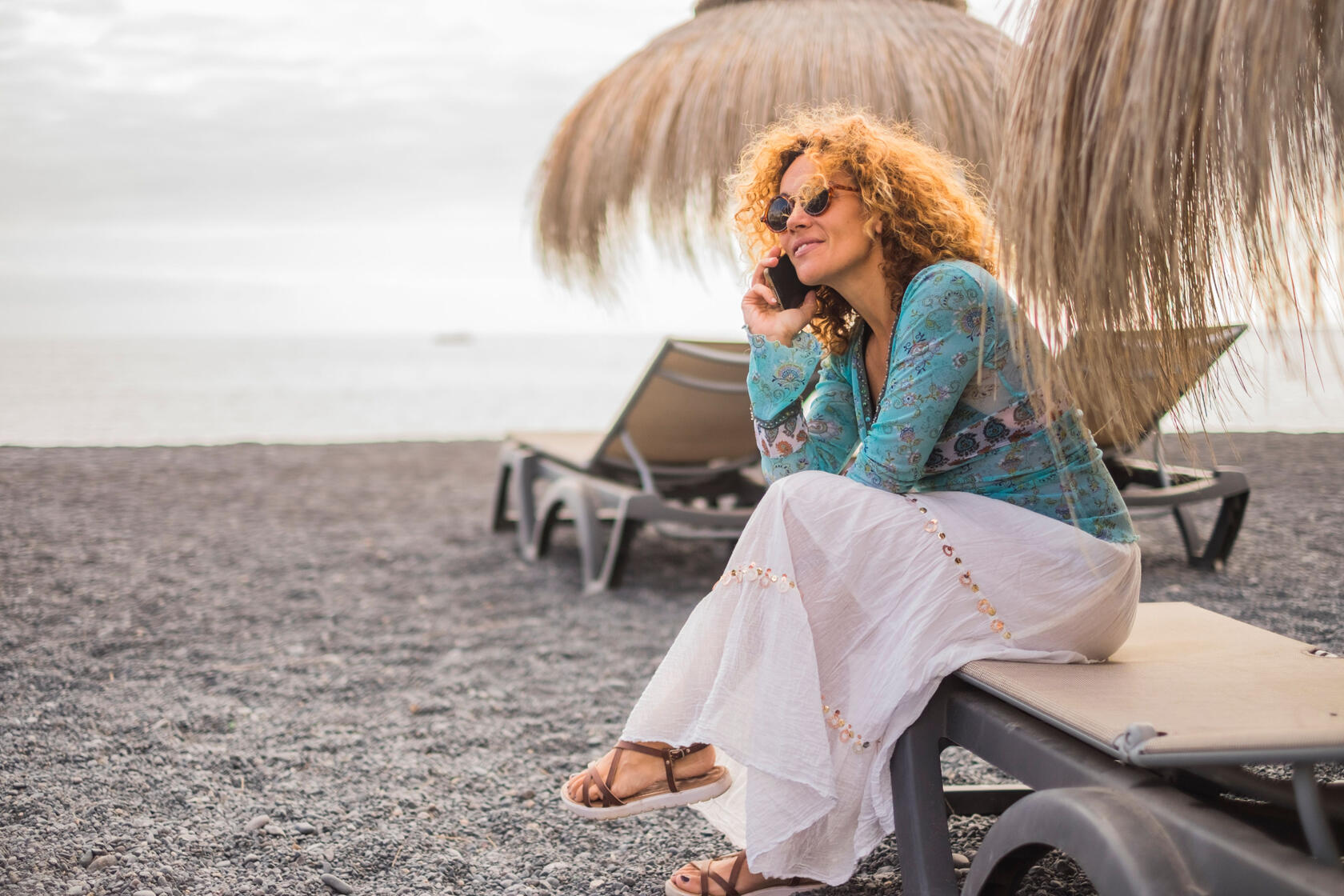 Woman sitting at the beach, talking on her phone Woman sitting at the beach, talking on her phone